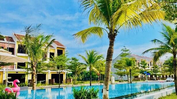 Area piscina di un resort con palme, un gonfiabile a forma di fenicottero rosa e un cielo azzurro terso.