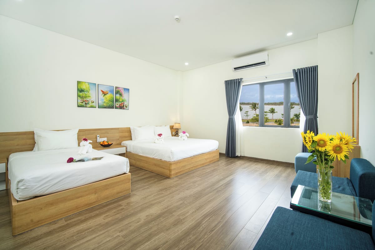 Habitación de hotel con dos camas, un sofá, una mesa de vidrio, un jarrón con flores y una ventana con cortinas.
