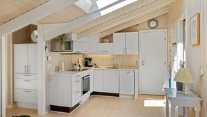 A modern kitchen with white cabinets, a microwave, and a sink. There is a clock on the wall and a plant on the counter. - 3 bedroom beautiful home in Blokhus (Blokhus)