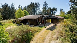 A rustic cabin with a covered porch and a small deck, surrounded by dense forest. - 3 bedroom beautiful home in Blokhus (Blokhus)