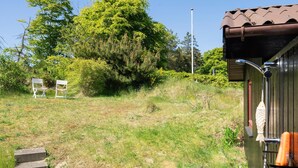 A grassy area with two white chairs, a wooden building with a metal roof, and a metal structure with a hose. - 3 bedroom beautiful home in Blokhus (Blokhus)