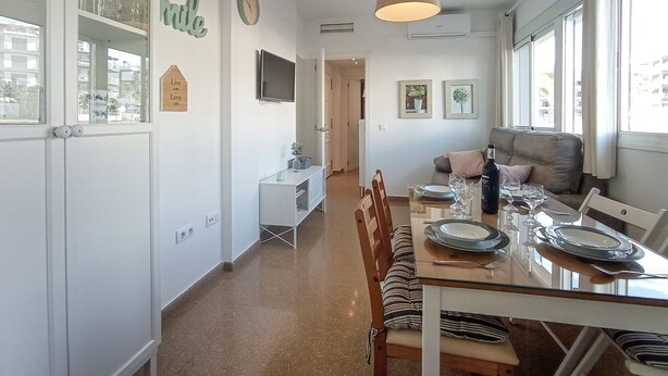 Une cuisine moderne avec des meubles blancs, une table à manger pour quatre personnes et un canapé dans l’espace salon.