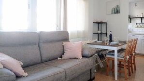 Un salon moderne avec un canapé gris, une table à manger dressée pour quatre personnes et, au fond, un coin cuisine.