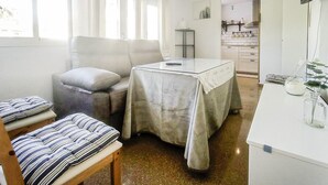 Un espace de vie compact comprenant un canapé, une petite table et un coin cuisine à l’arrière-plan.