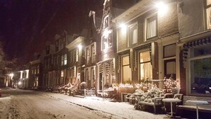 Een besneeuwde straat met gebouwen aan beide zijden, met grote ramen en enkele terrassen.