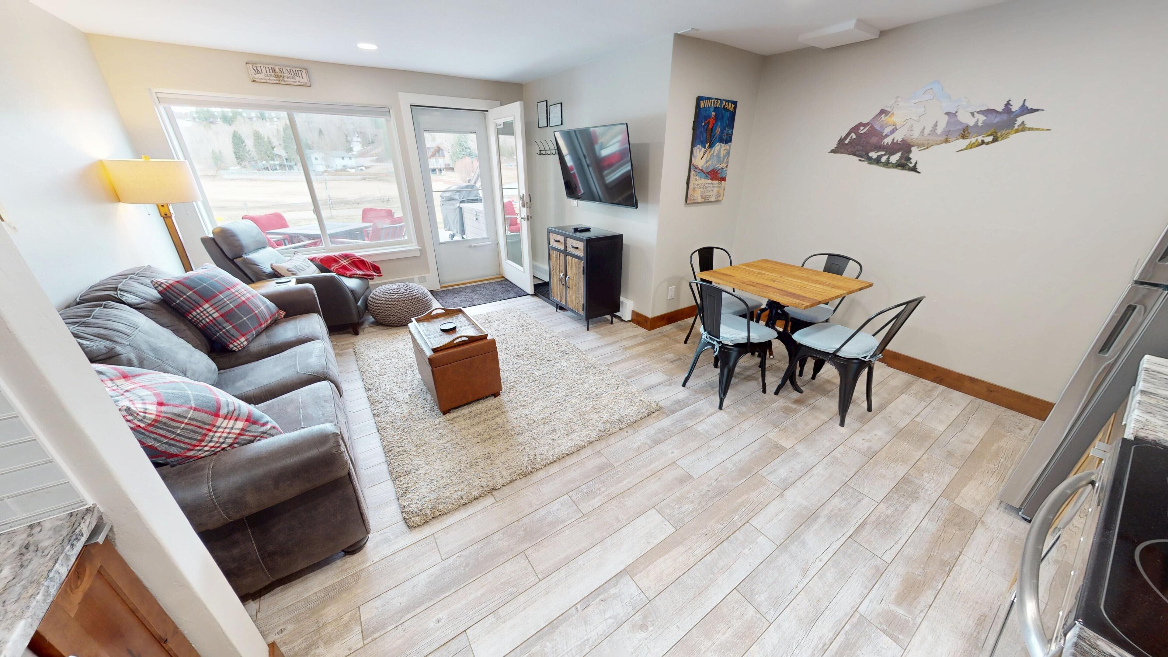 A living room with a sofa, a coffee table, a TV, and a dining area with a table and chairs.