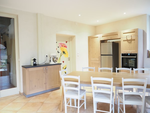 A modern kitchen with wooden cabinets, a built-in oven, and a dining table with white chairs. - 1860 farmhouse with mill - nature, peace & quiet & hiking in the heart of the Vosges mountains (Le Thillot)