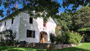 Una casa blanca con un muro de piedra, una puerta de madera y una ventana con contraventanas de madera.