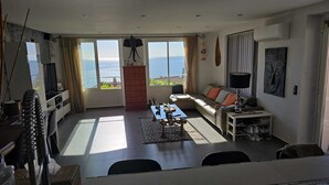 Amplia sala de estar con un ventanal que ofrece vistas al mar, un sofá, una mesa de centro y un televisor.