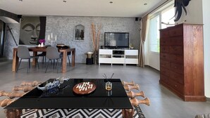 Una sala de estar moderna con comedor, televisor y un amplio ventanal.