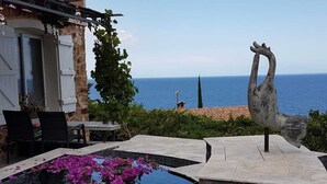 Una piscina con flores moradas, una escultura y vista al mar.