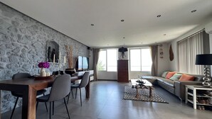 Un salón amplio con una pared de piedra, una mesa de comedor con sillas, un sofá y un televisor.