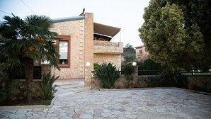 A stone building with a balcony, surrounded by a stone-paved courtyard and palm trees. - Neriana Villa - Garden Paradise (Chania)