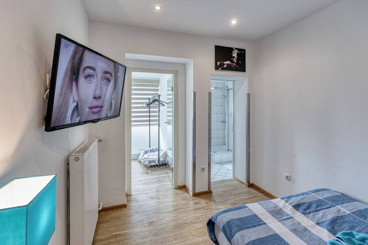 Ein modernes Schlafzimmer mit einem Bett, einem an der Wand montierten Fernseher und Blick ins Bad.