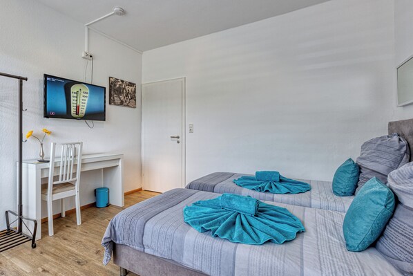 A bedroom with two beds, a desk, a chair, and a television on the wall.