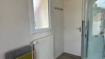 Un baño con mampara de vidrio, radiador blanco, ventana con cristal satinado y un perchero con una toalla verde.