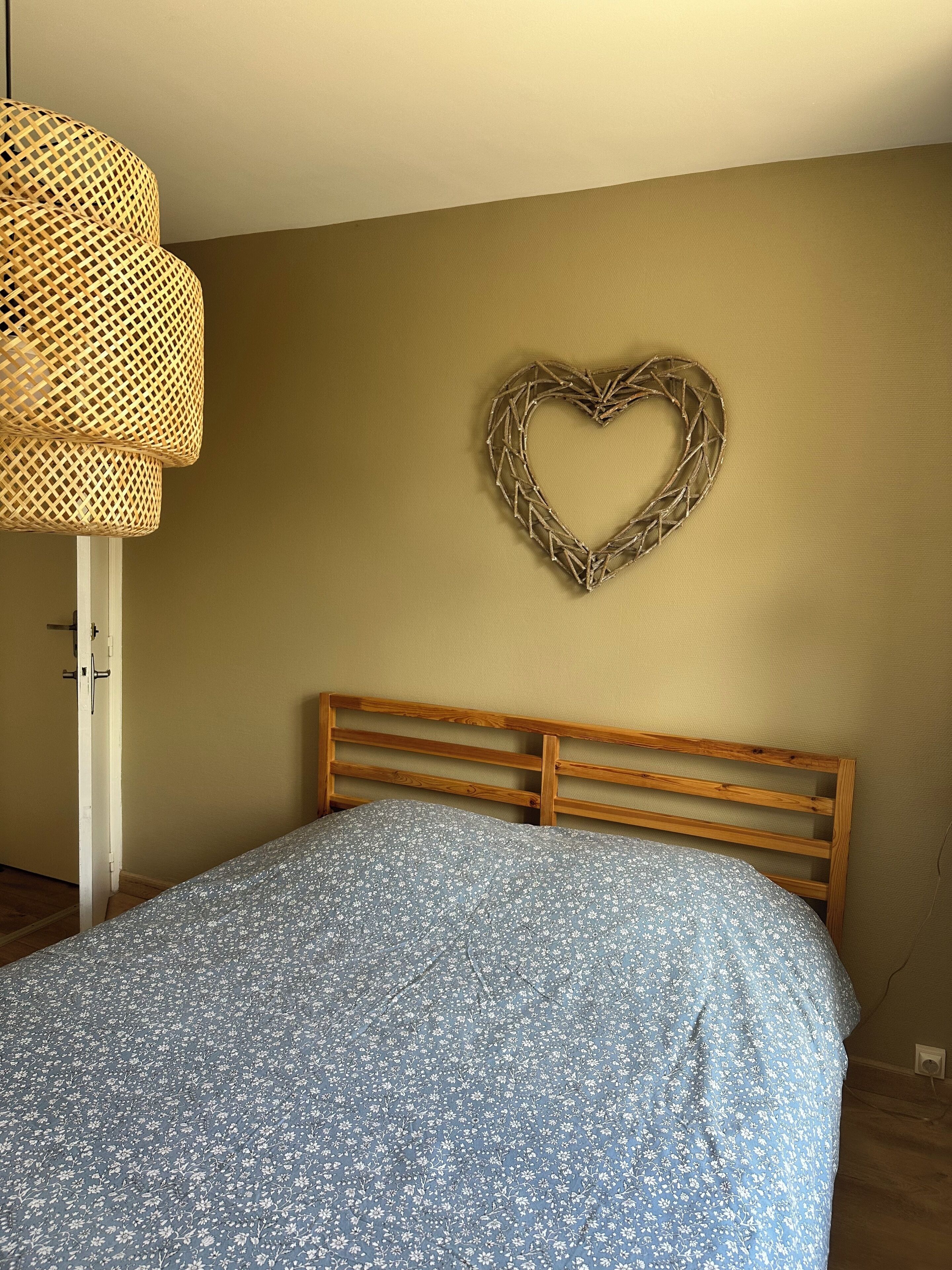 A bedroom with a wooden headboard, a floral-patterned bedspread, a woven wall hanging, and a door with a white frame.