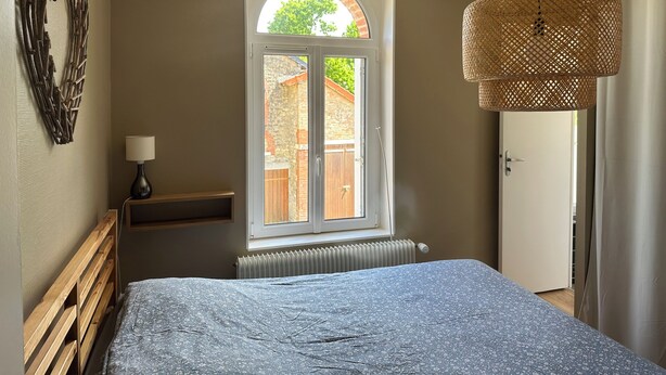 A bedroom with a bed, a window, a radiator, a lamp, and a wicker lamp.