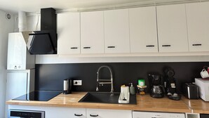 A modern kitchen with white cabinets, a black countertop, a stainless steel sink, and various appliances including a coffee maker and a toaster.