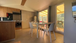 Una cocina moderna con armarios de madera, un comedor con sillas blancas y un amplio ventanal corredera que da a una terraza al aire libre.