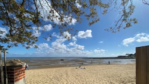 Una playa arenosa con una estructura de madera a la izquierda y un cielo azul despejado con nubes.