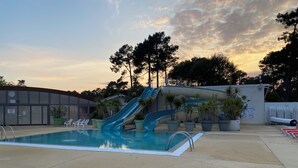 Una piscina con dos toboganes, rodeada de plantas en macetas y un edificio con un letrero.