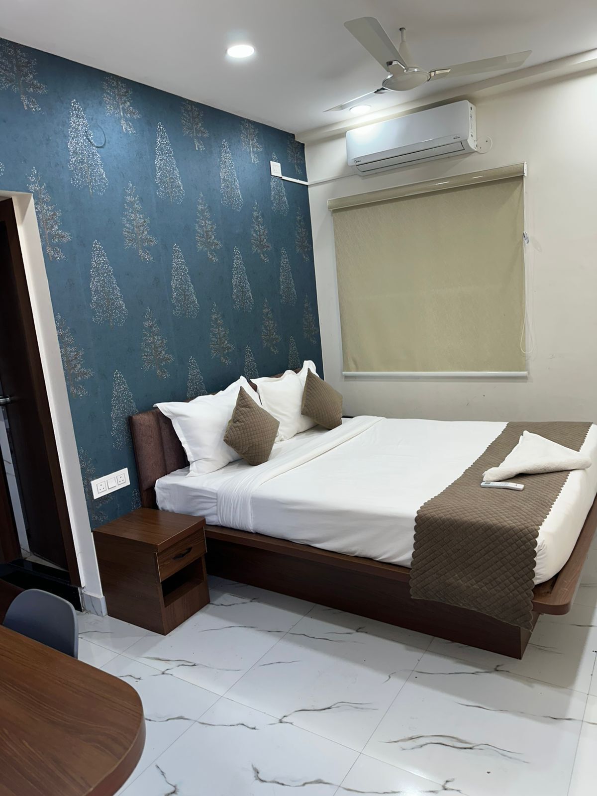 A bedroom with a bed, a bedside table, a wardrobe, a ceiling fan, an air conditioning unit, and a window with a blind.