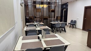Un espace de restauration moderne, doté de tables et de chaises, d’un ventilateur de plafond et offrant une vue sur un restaurant grâce à une paroi vitrée.