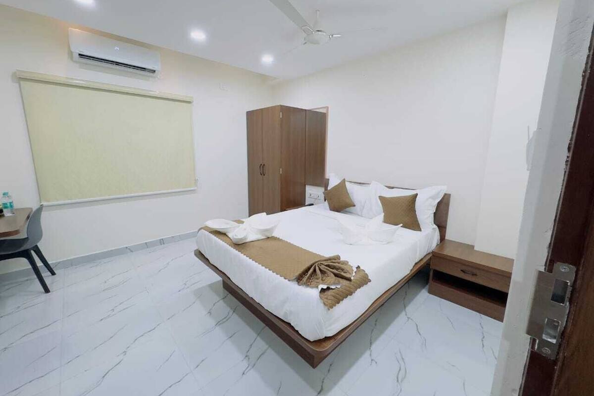 A hotel room with a bed, bedside table, wardrobe, and an air conditioning unit.