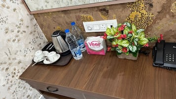A wooden desk with a kettle, water bottles, a tissue box, a phone, and a decorative plant.