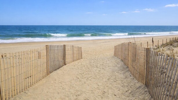 A sandy beach path leading to the ocean, bordered by wooden fences.