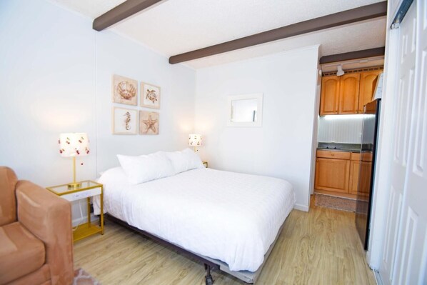 Un dormitorio con una cama, lámparas de noche, una mesita de noche, una silla y vistas a una cocina.