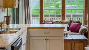 A kitchen with wooden cabinets, a sink, and a window overlooking a green landscape.