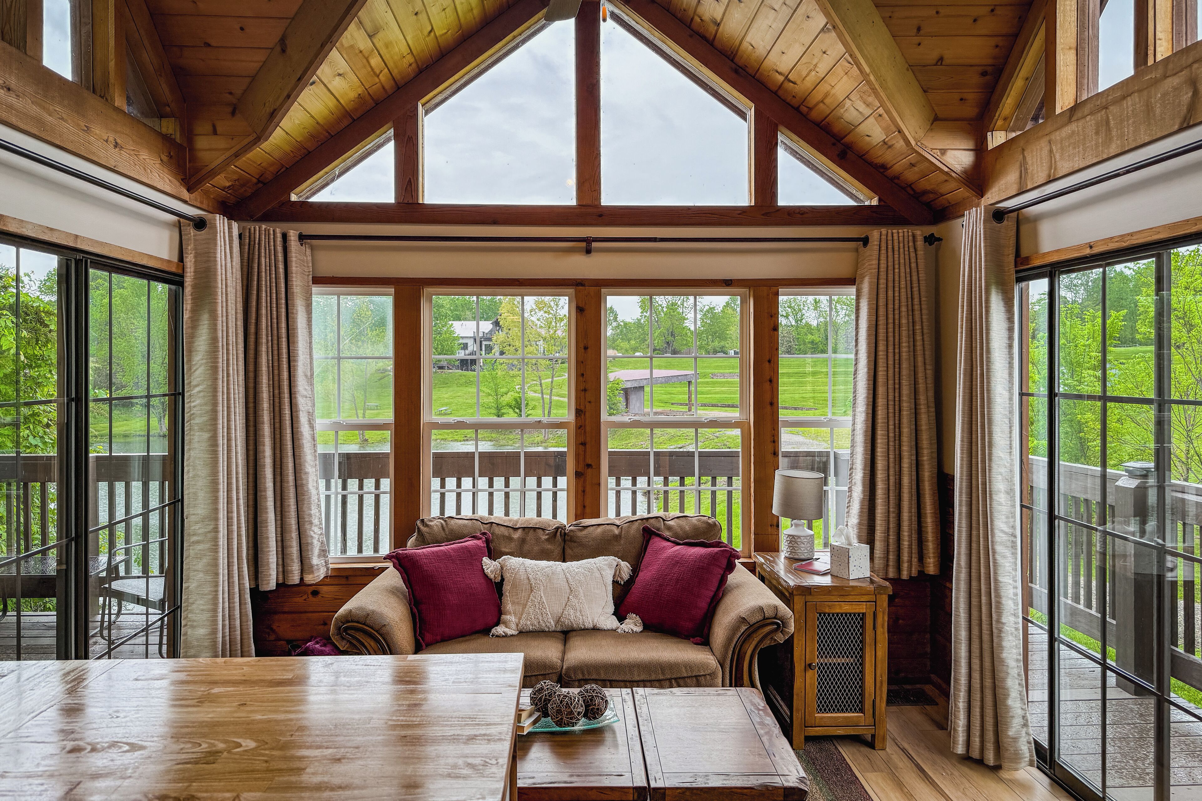 Una habitación acogedora con techo de madera, ventanas amplias, una mesa de madera y un rincón de estar con cojines.