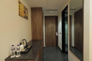 A hotel corridor with a wooden door, a mirror, and a counter with bottled water and a kettle. - SNJ TAJ GRAND HOTEL (Agra)