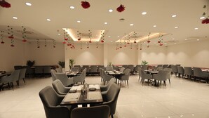 A spacious dining area with multiple tables and chairs, ceiling lights, and hanging decorations. - SNJ TAJ GRAND HOTEL (Agra)