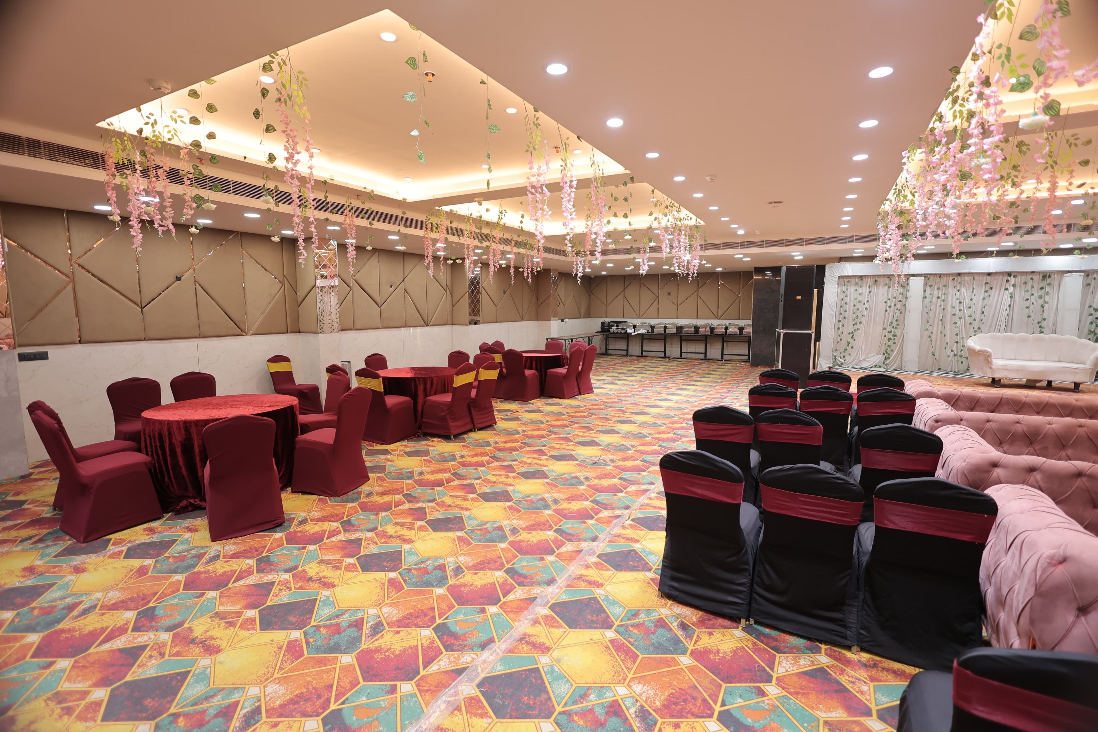 A banquet hall with round tables and chairs, a patterned floor, and hanging floral decorations.