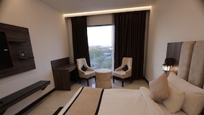 A hotel room with a large bed, two armchairs, a small table, a TV mounted on the wall, and a window with curtains. - SNJ TAJ GRAND HOTEL (Agra)