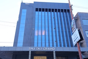 Un edificio moderno con la segnaletica 'SNJ TAJ GRAND', che indica un hotel o struttura simile.