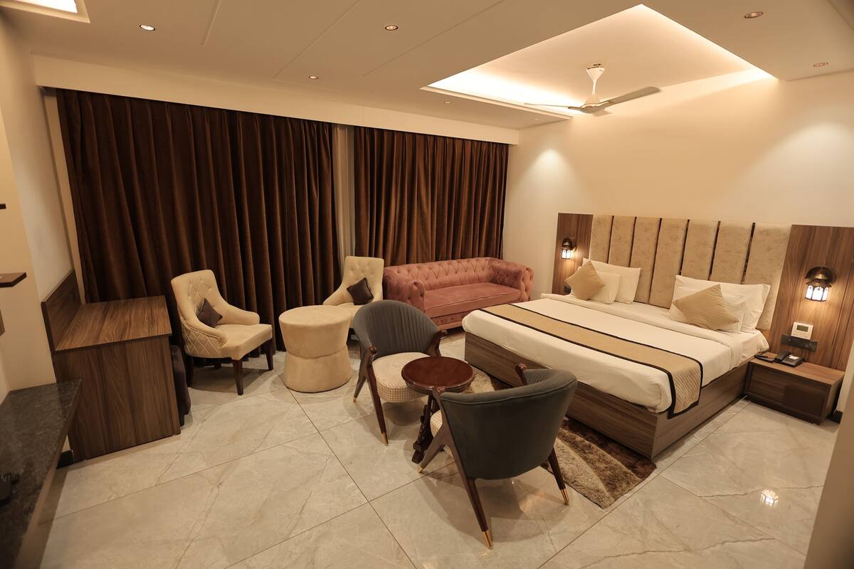 A modern bedroom with a large bed, a desk, two armchairs, a sofa, and a ceiling fan.