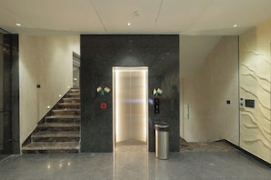 A modern lobby with a marble floor, a staircase, an elevator, and a trash bin. - SNJ TAJ GRAND HOTEL (Agra)