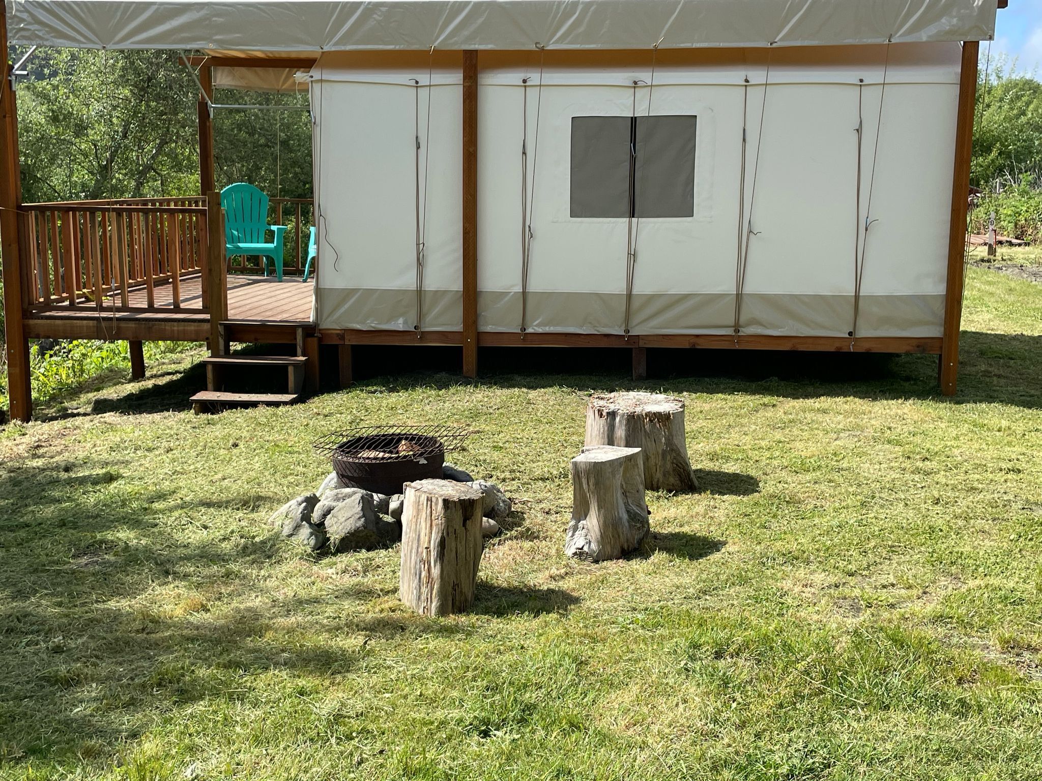 A camping site with a large tent, a fire pit, and two wooden stumps.