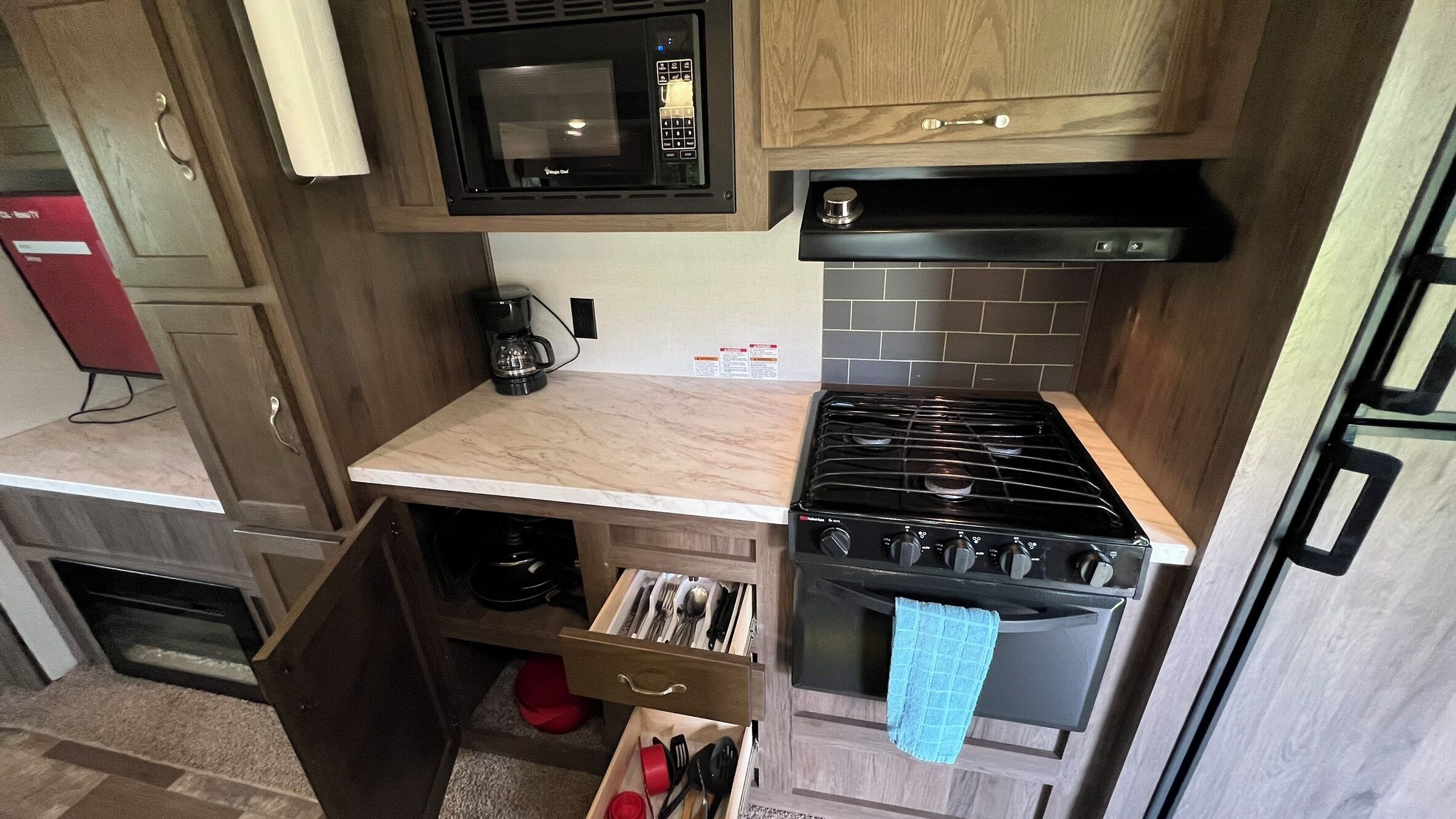 A compact kitchen with a microwave, stove, and drawer with utensils.