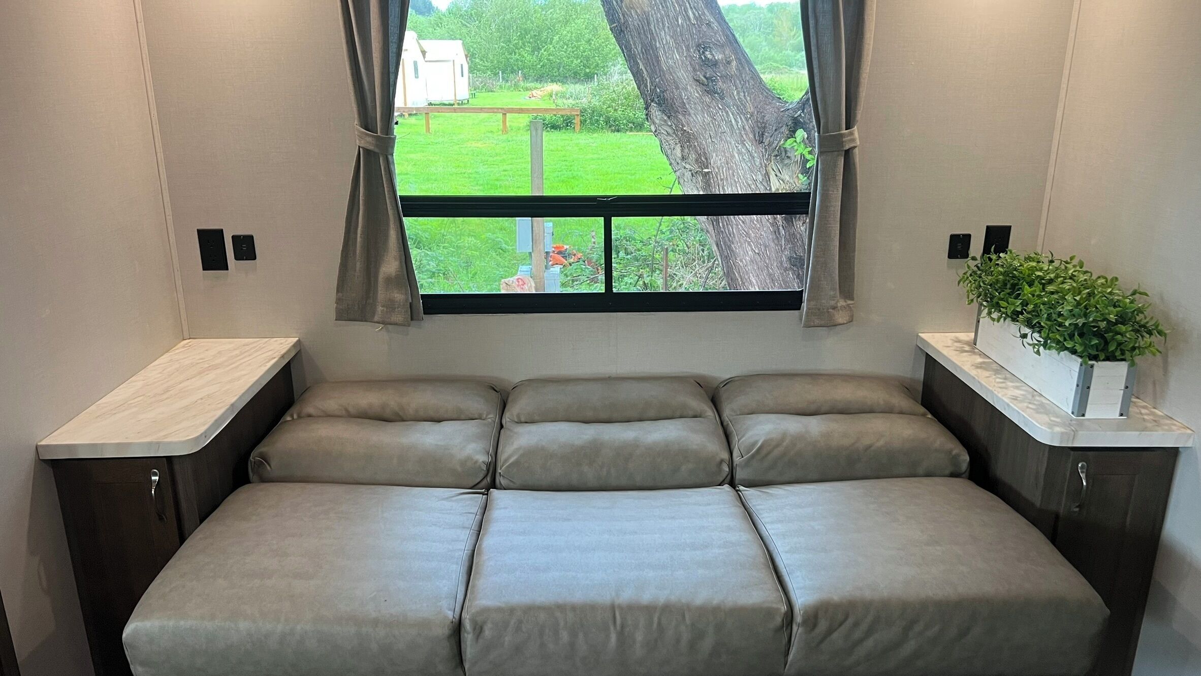 Un lit compact donnant sur un paysage verdoyant, visible à travers une fenêtre.
