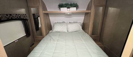 A compact bedroom with a bed, a small shelf with a plant, and a wardrobe.