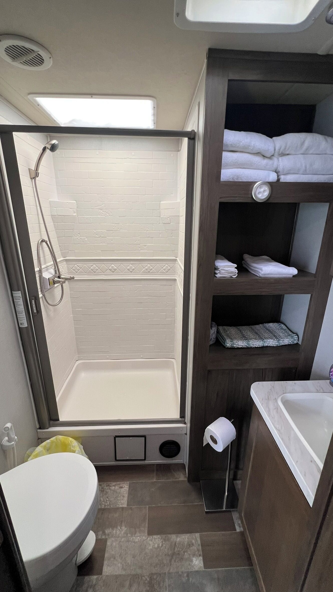 A compact bathroom with a shower, toilet, and a shelf with towels.