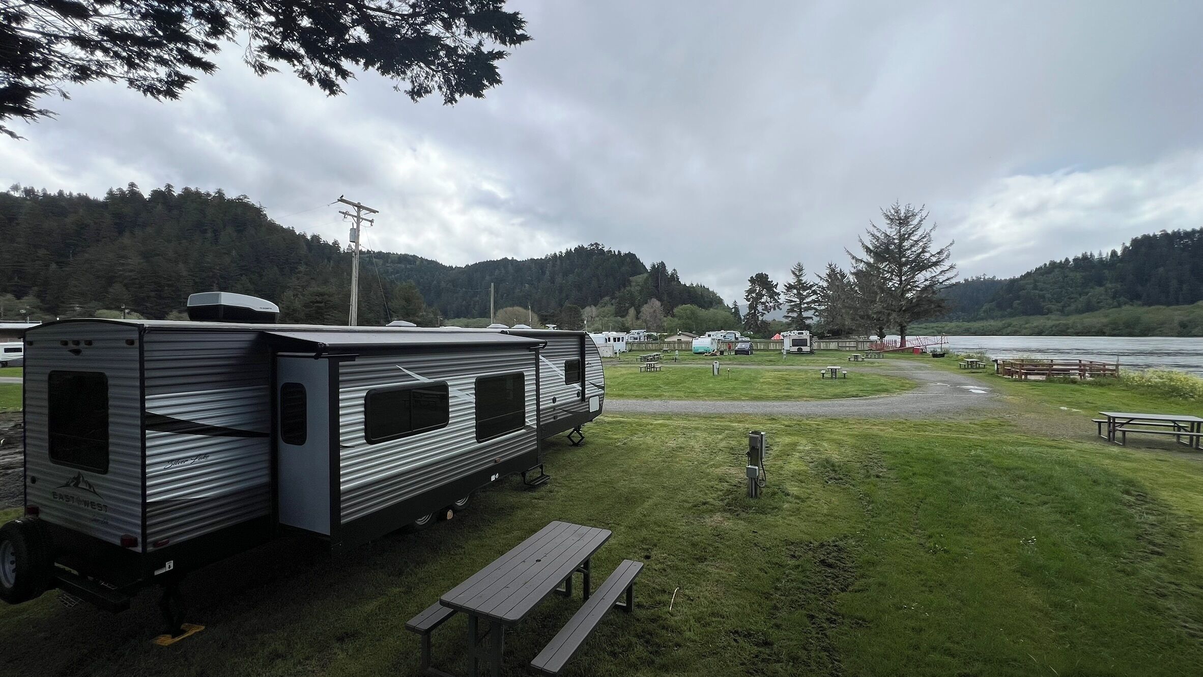A campsite with RVs, picnic tables, and a lake view.
