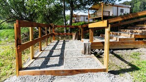 A wooden deck with a gravel floor, surrounded by trees and a white building in the background.