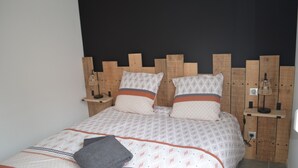A bed with patterned bedding, two pillows, a bedside table with a lamp, and a wall-mounted shelf. - Country cottage (Raon-aux-Bois)