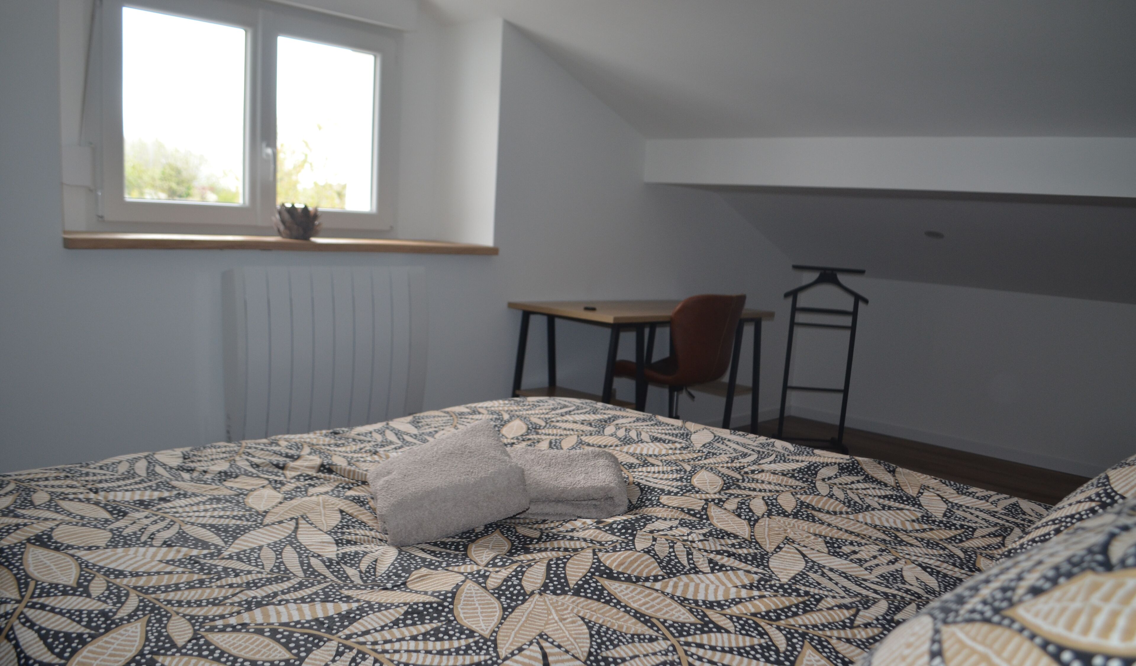 A bedroom with a bed, a chair, a desk, and a radiator.